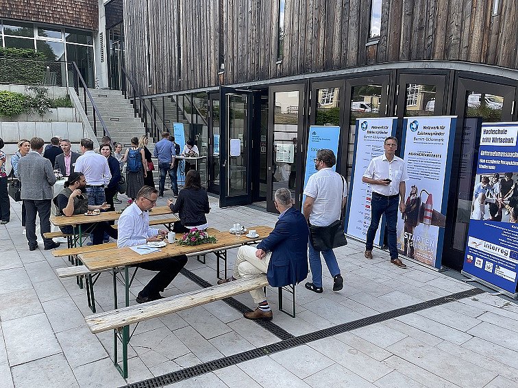 Menschen sitzen an Tischen und reden. Menschen stehen in Grüppchen zusammen und reden.
