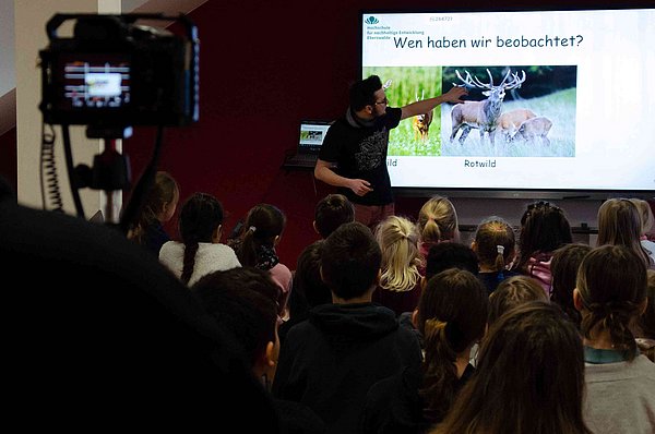 Ein junger Mann erklärt etwas in seiner Präsentation. Die Kinder hören zu