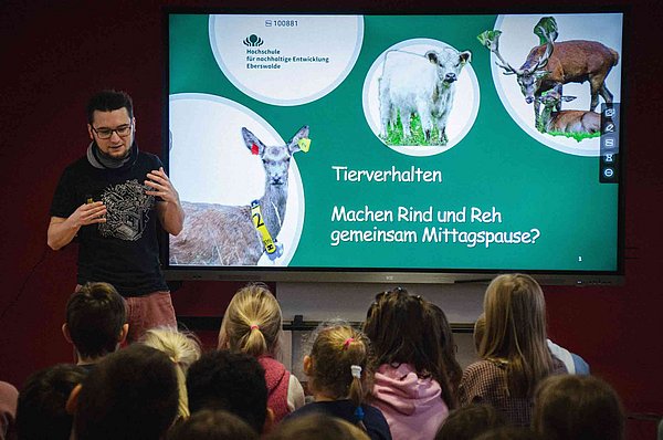 Ein junger Mann steht vor Schulkindern und erklärt Tierverhalten in seinem Science Slam